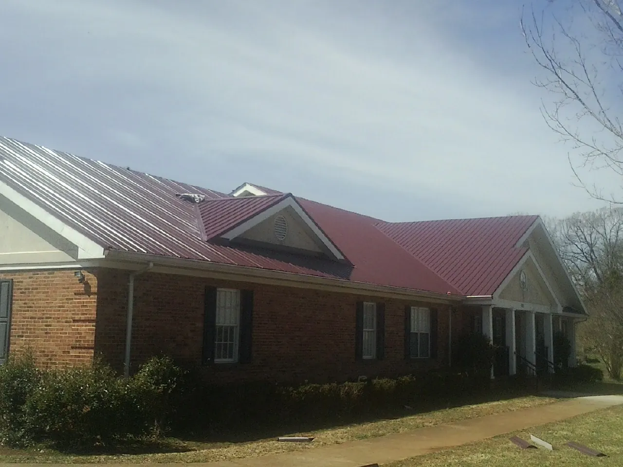 Red metal roof with gabled entries on a long brick building, from a Hail Damage Roof Repair job in Glen Alpine