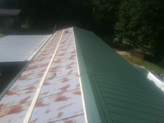 Old rusted panels beside newly installed green metal roofing — Wind Damage Roof Repair by Roofing Brothers in Glen Alpine