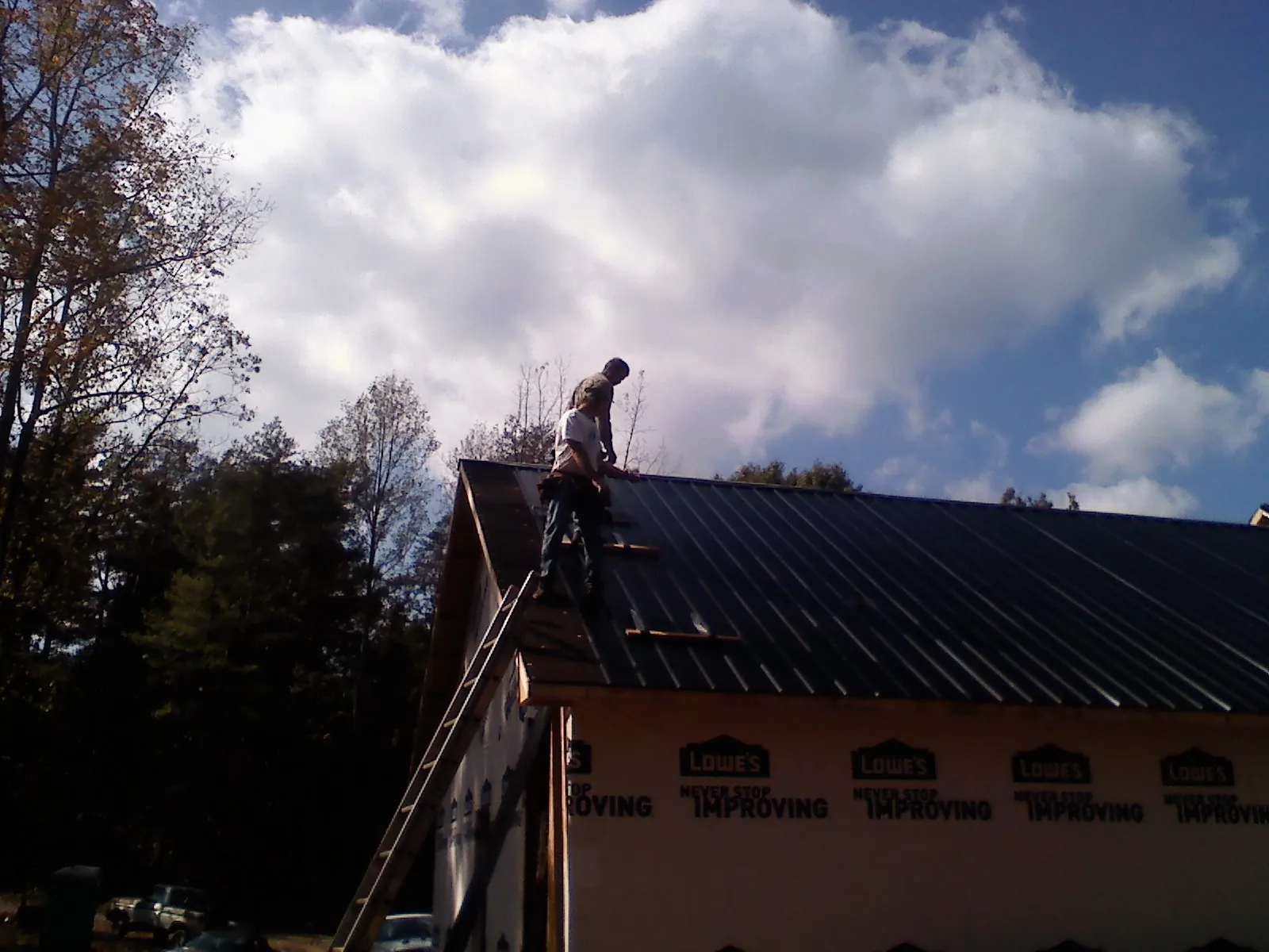 Roofer fastening dark metal panels high against a cloudy sky, from a Roof Inspection job in Glen Alpine