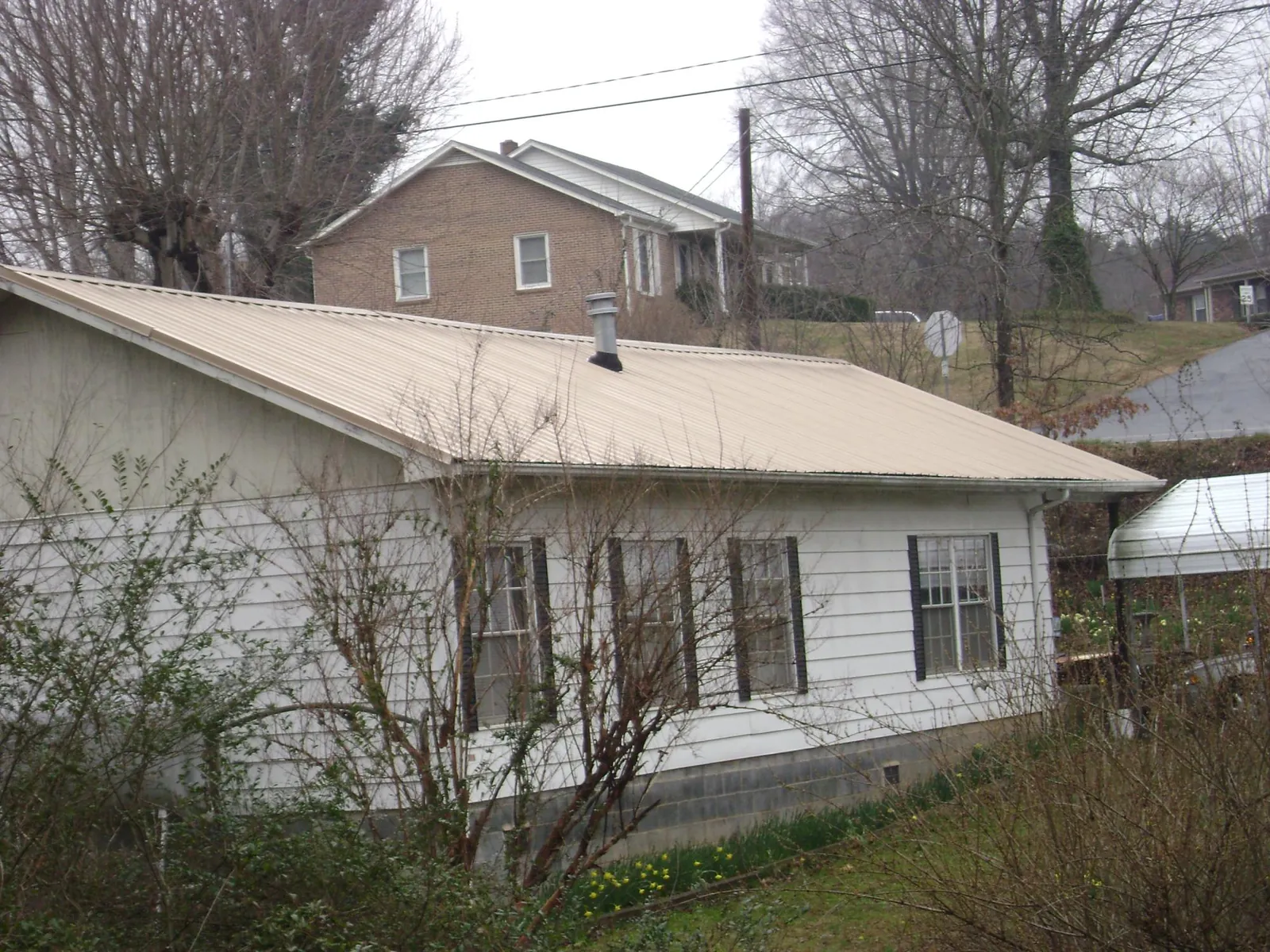 Tan metal roof on a white sided house set into a hillside — Commercial Roofing by Roofing Brothers in Glen Alpine